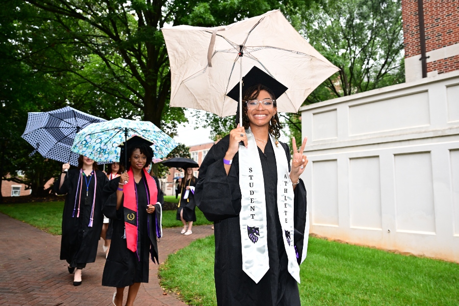 A graduate walks to the ceremony while holding an umbrella