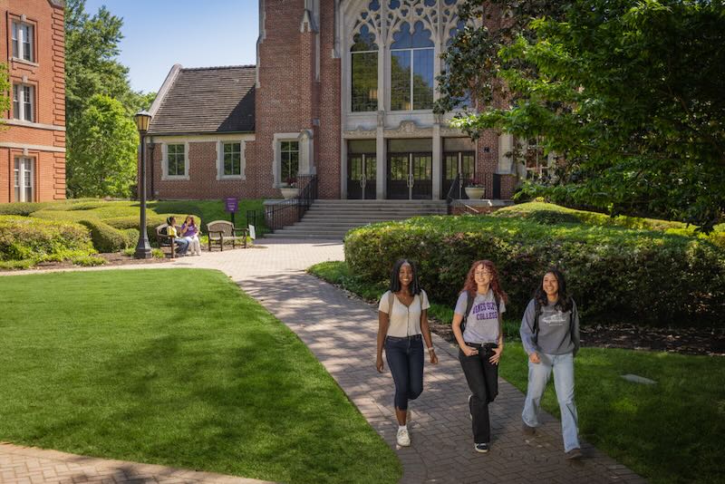 Three Agnes Scott students smiling and walking across the campus on a sunny day