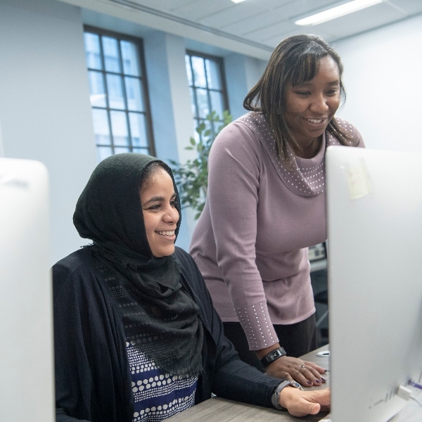 Two digital media graduate students looking at a computer screen and smiling.