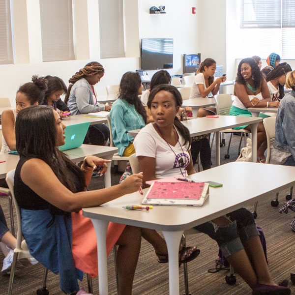 A class room full of Agnes Scott College students talk amongst each other.