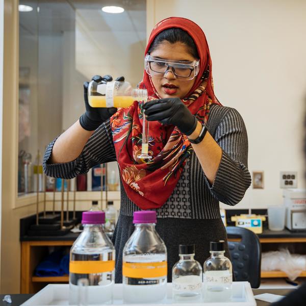 A chemistry major student wearing a colorful hijab pours a solution into a test tube.