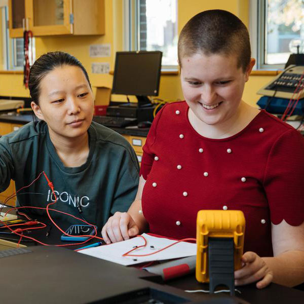 Two computer science major student's reading a device's output and taking notes.