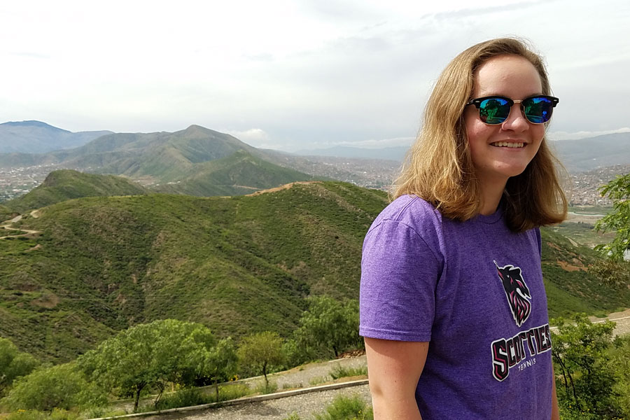 Agnes Scott study abroad student wearing sunglasses and smiling on top of a green mountain in Bolivia.