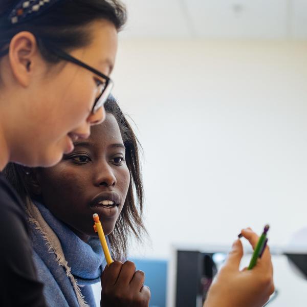 Two Agnes Scott physics major students hold and look closely at a small metal object.