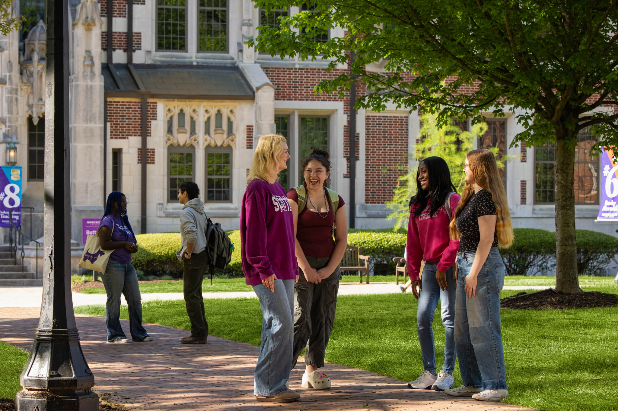 Six students standing in two groups on the campus quad and talking and laughing