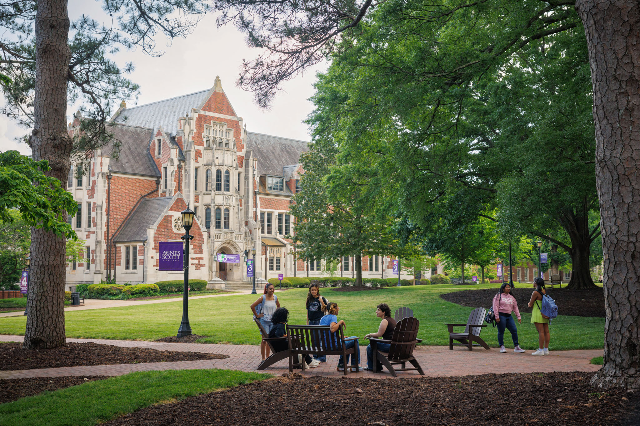 Six students on the quad, some sitting in chairs and some standing, while they talk