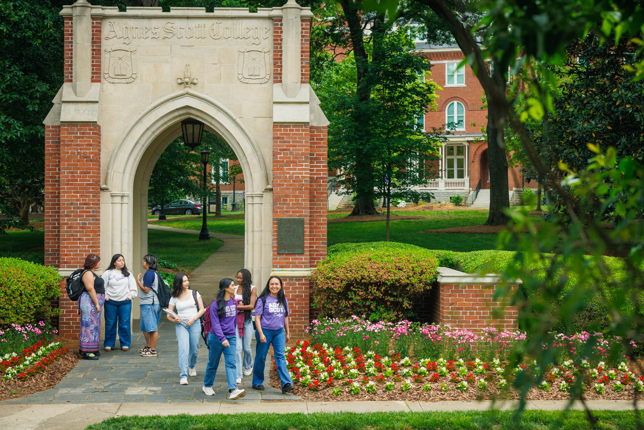 Students walking out of the Agnes Scott arch, surrounded by foliage and flowers in bloom