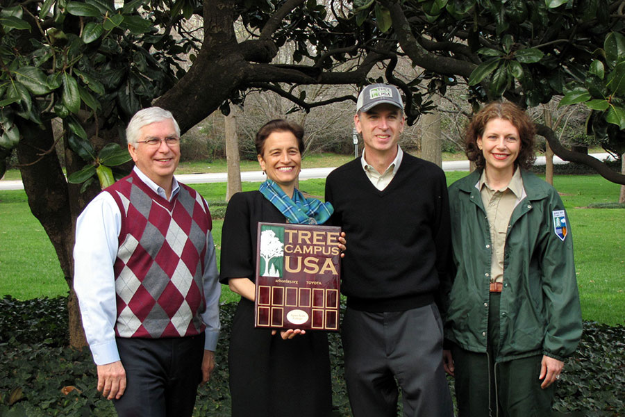 College leaders and others standing with a Tree Campus USA sign under a magnolia tree