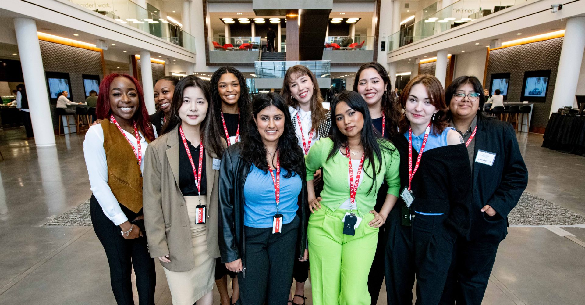 A group of Agnes Scott College students wearing visitor badges pose for a photo inside the Mercedes-Benz USA headquarters during a SCALE program experience.