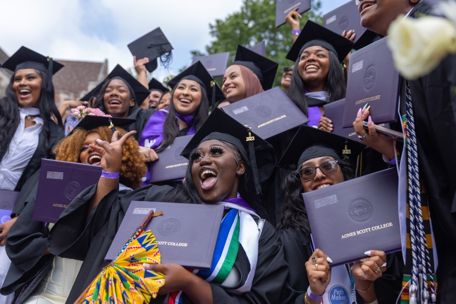 A group of students gather for a photo while holding their purple diplomas