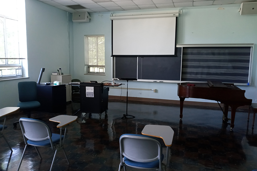 View of Presser 202 showing desks, lectern, projection screen, baby grand piano, and chalkboard with musical staff