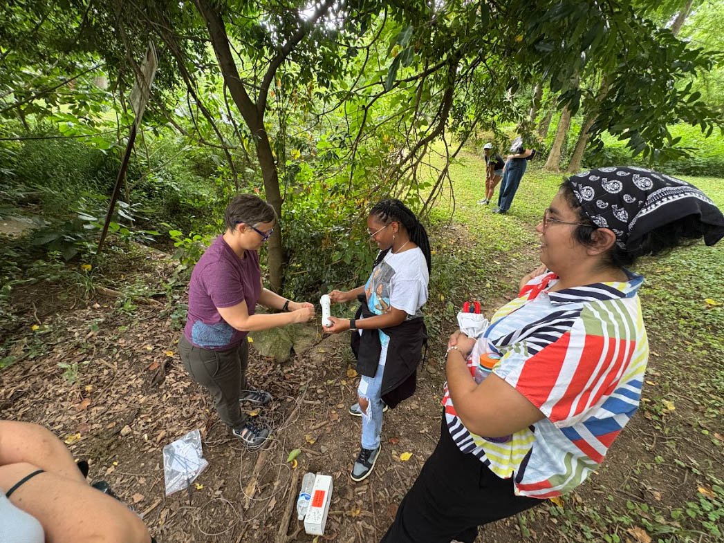 two students in the field with a faculty training how to use a stream sensor