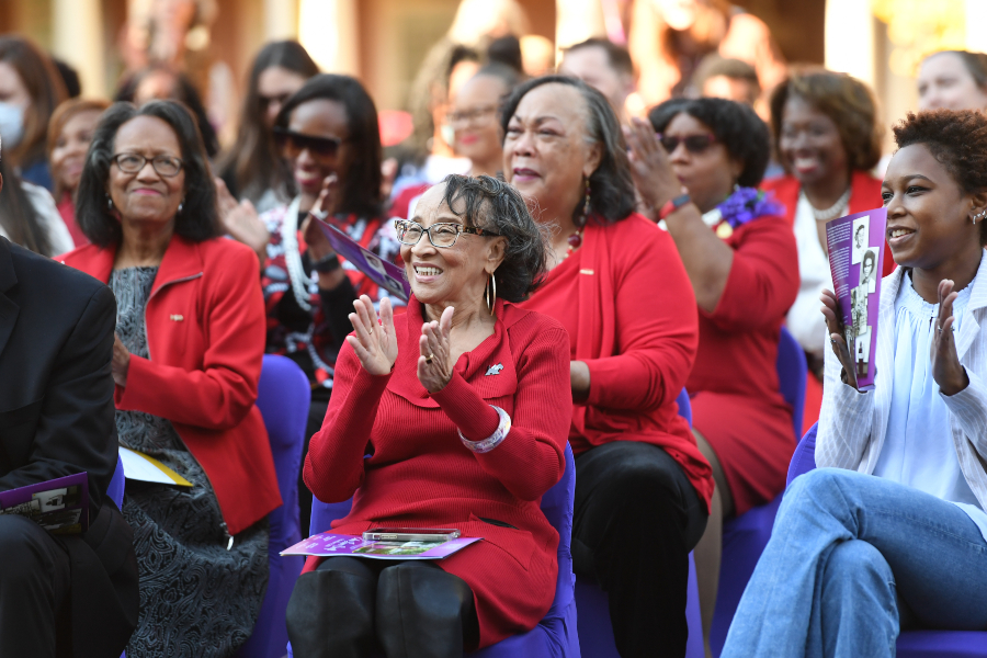 a group of women wearing red sweaters clap for the performers standing ahead out of focus
