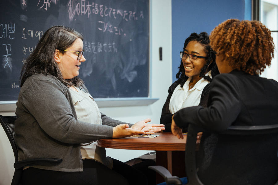 three adults sit at a round table in a classroom having a jovial discussion