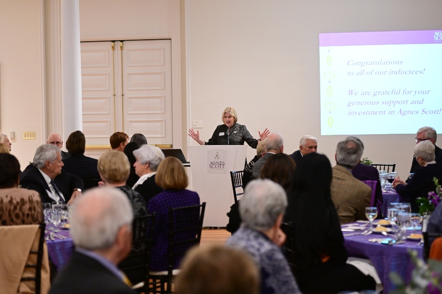 An important person stands a podium in front of a large group of people seated a tables