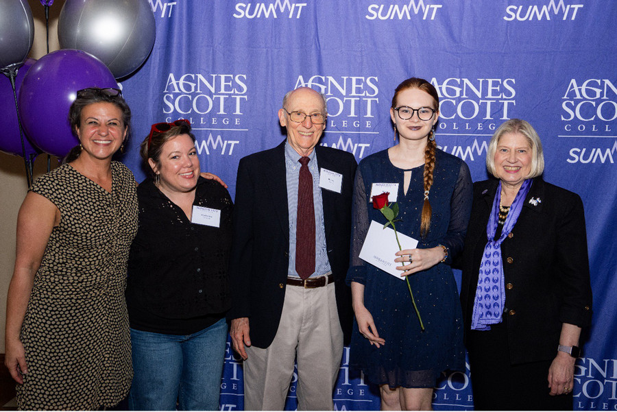 Two Agnes Scott College student award recipients stand with donors and college representatives during the 2026 Student Award Celebration. The students hold red roses and award materials while posing for a photo in front of the event backdrop.