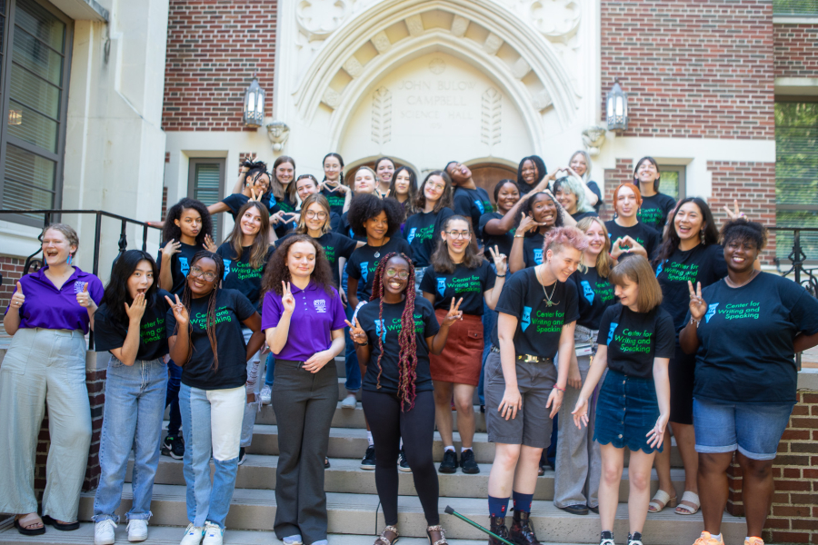 a group of student tutors gather on building stairs wearing the same branded black tee shirts