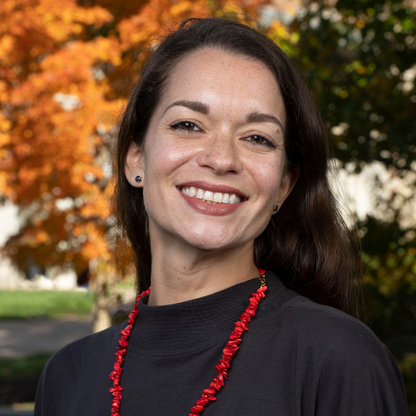 a professor wearing a black sweater and bright red necklace smiles at the camera
