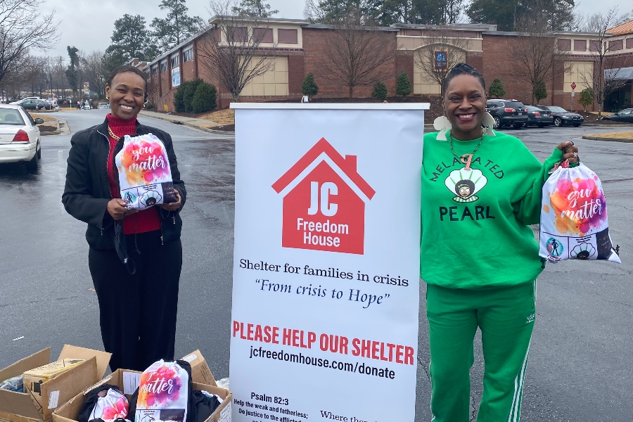 Crystal Perry stands with a Freedom House employee in front of a white sign of the non-profit. 