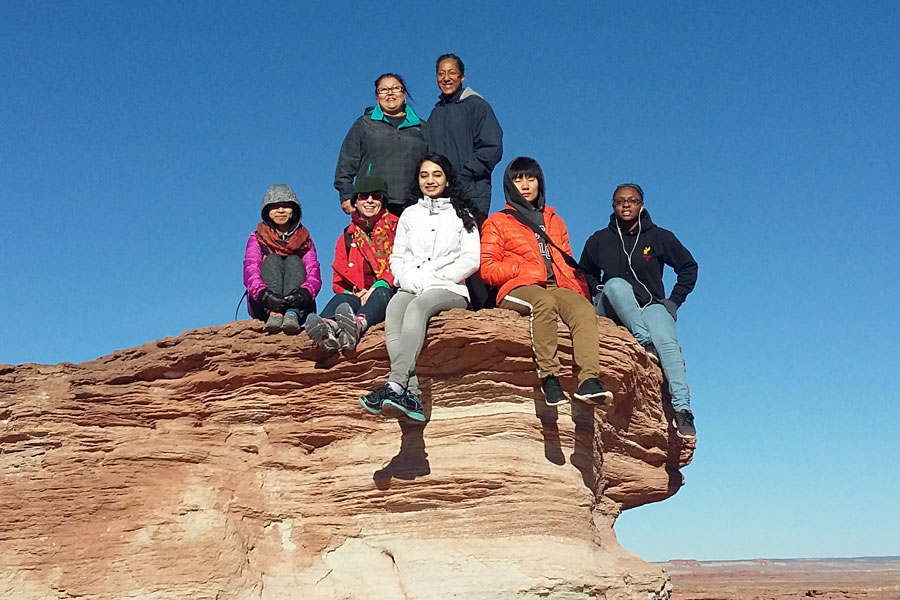 A group of students pose for a photo on a rock formation in the Navajo Nation.