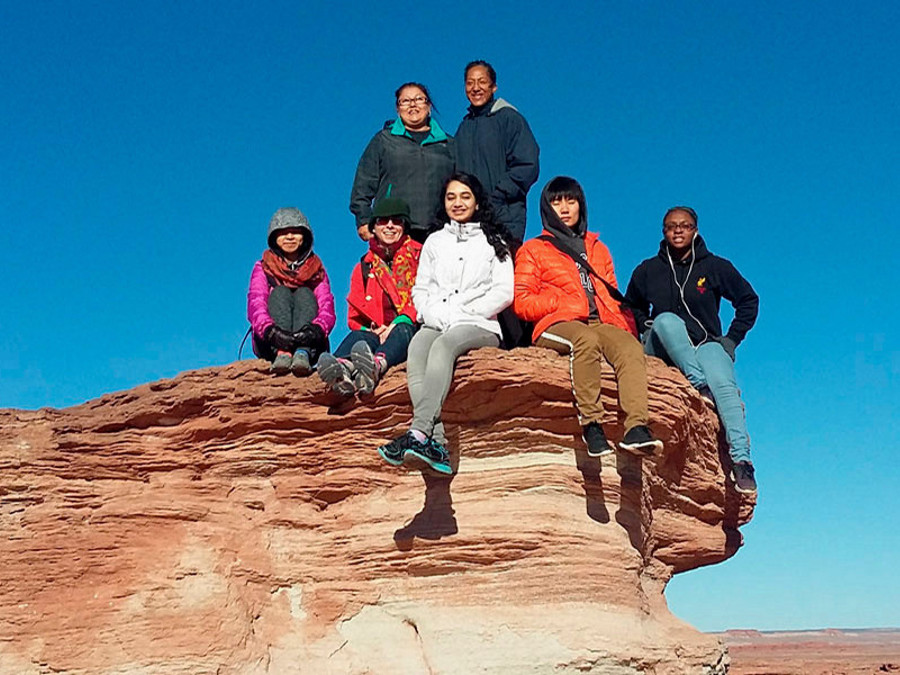 A group of students pose for a photo on a rock formation in the Navajo Nation.